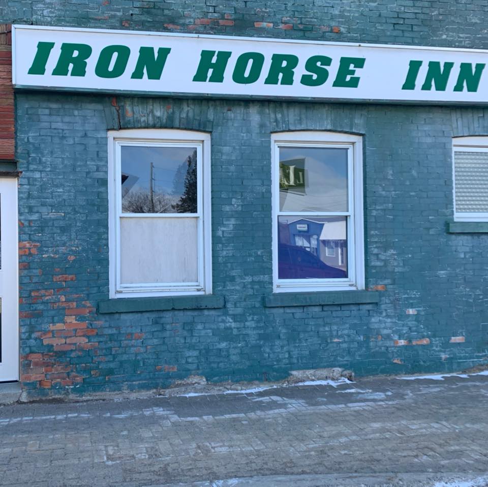 The Iron Horse Inn has a new white sign with green lettering and new windows. The building is brick, painted teal, with a little bit of paint coming off. 