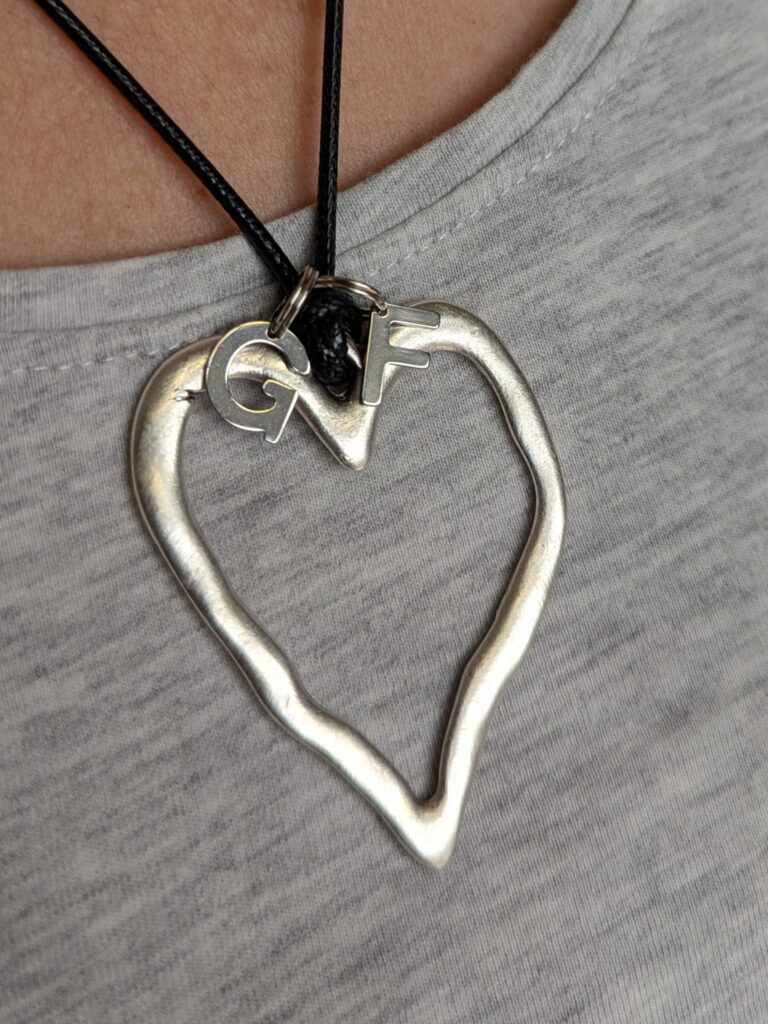close-up of a silver-toned heart pendant with a silver G on one side and an F on the oether