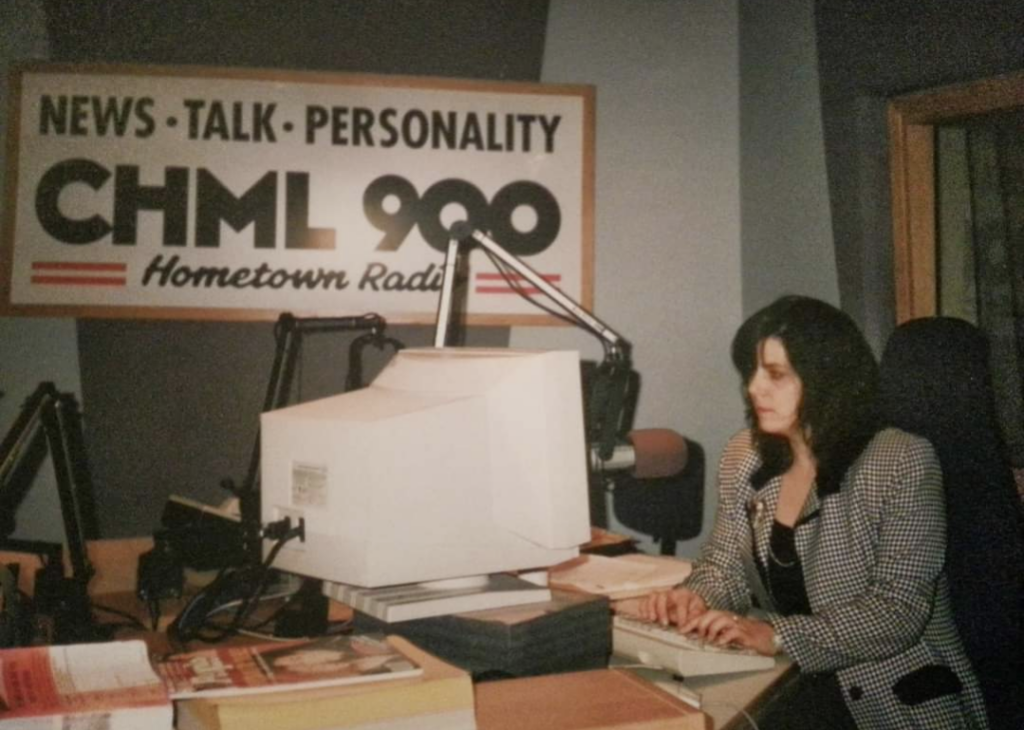 Lisa typing madly and looking serious in the CHML on air studio with the call letters on a sign in the background.