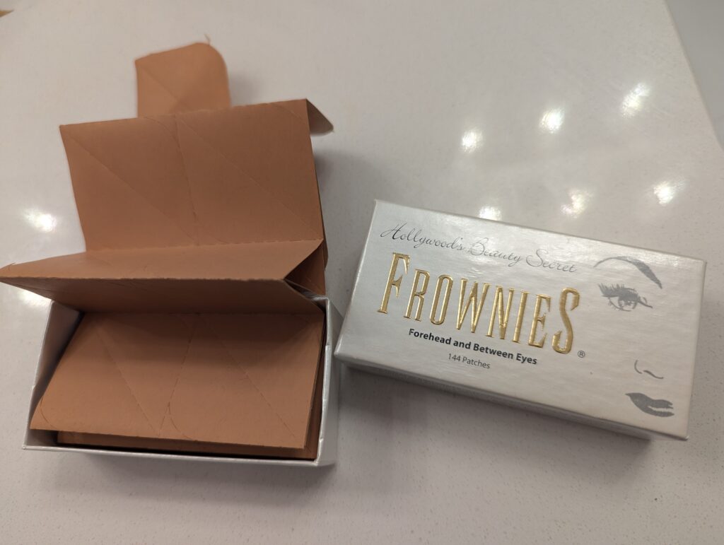 An open box of "Frownies - Hollywood's Beauty Secret". Brown stickers come in a never-ending tear-away package. 