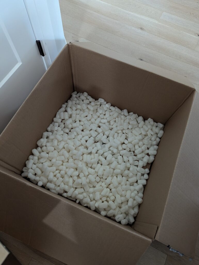 A large cardboard box with a couple of inches of packing peanuts in the bottom.