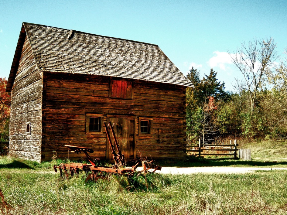 Old wooden farmhouse looks like it's one room and has a split rail fence beside it.