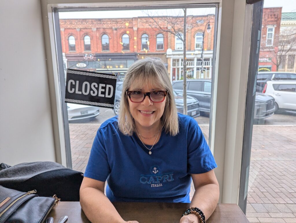 Me, smiling at Derek as we sit at a table waiting for breakfast. Behind me, is early 1900s architecture of the stores across the street. 