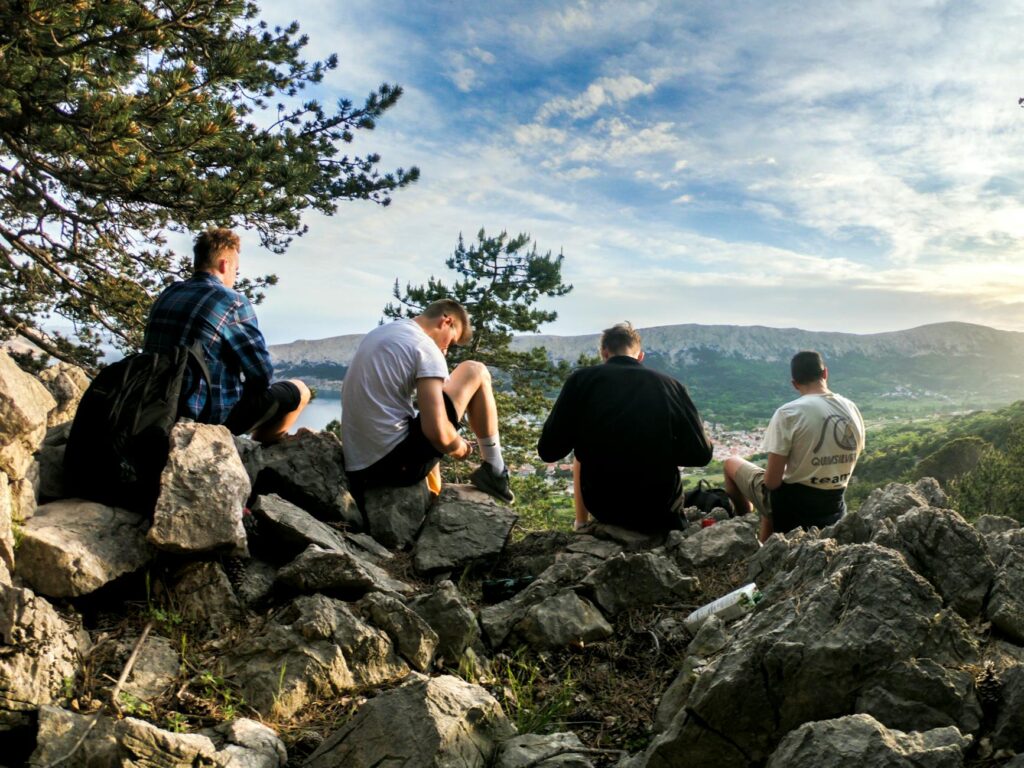 four men seated on rocks facing mountain