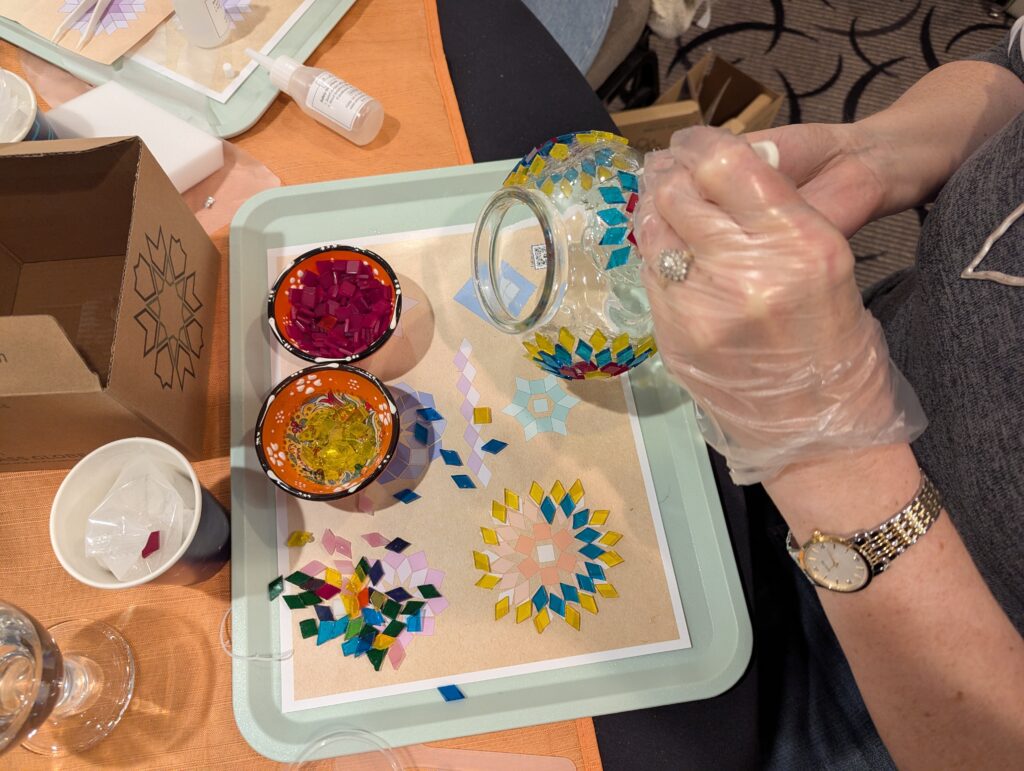 Carolyn's gloved hand is holding a big set of plastic tweezers. She's placing a blue diamond-cut tile onto the gluey glass globe. 