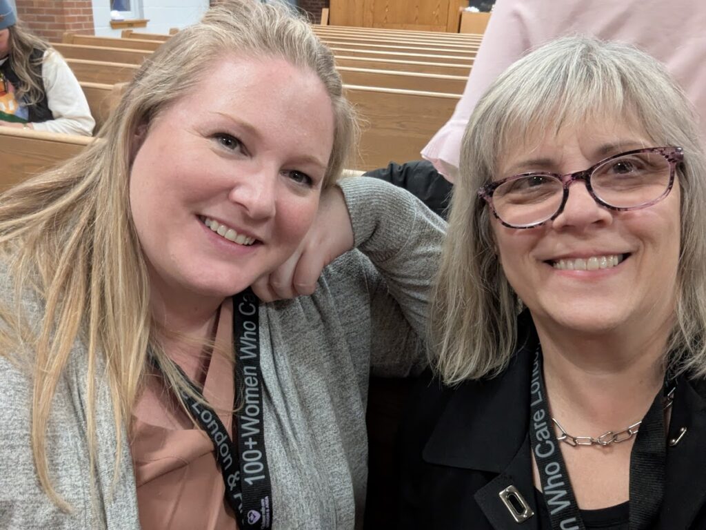 A 40-something blond woman and I smile into the camera. Church pews can be seen in the background.