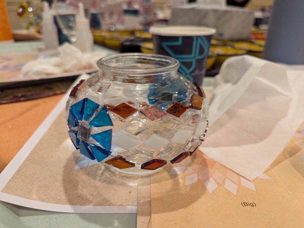 My globe after the big tiles were glued on. It has a square pattern of blue tiles meeting a centered mirror tile on either side. These main designs are joined by a band of diamond tiles in copper, clear, and white. 